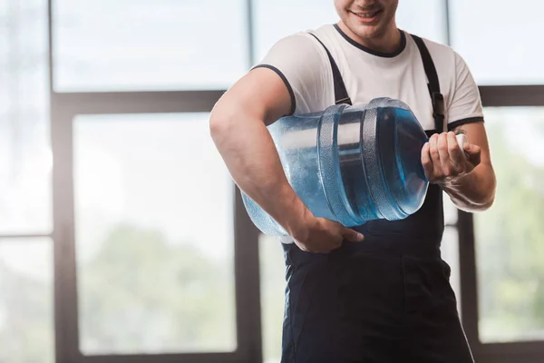 Cropped view of happy delivery man in uniform holding bottled water — Stock Photo