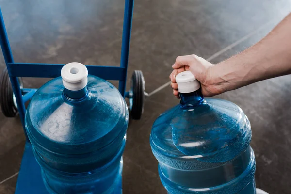 Vista recortada del repartidor hombre tocando botella con agua cerca de camión de mano — Stock Photo