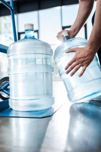 Vista recortada de repartidor hombre celebración botella con agua cerca de camión de mano - foto de stock