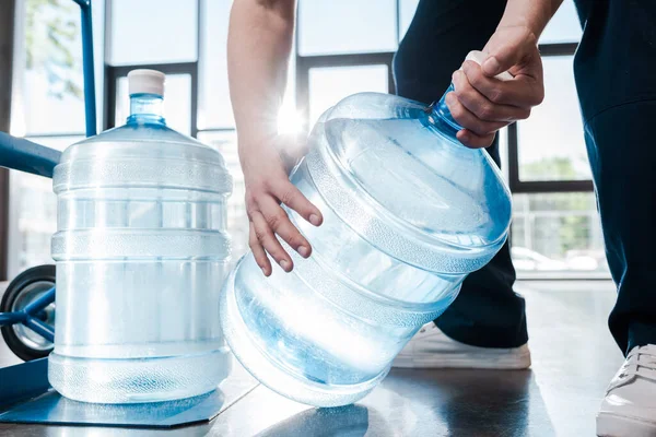 Vista recortada del repartidor hombre sosteniendo botella azul con agua cerca de camión de mano - foto de stock