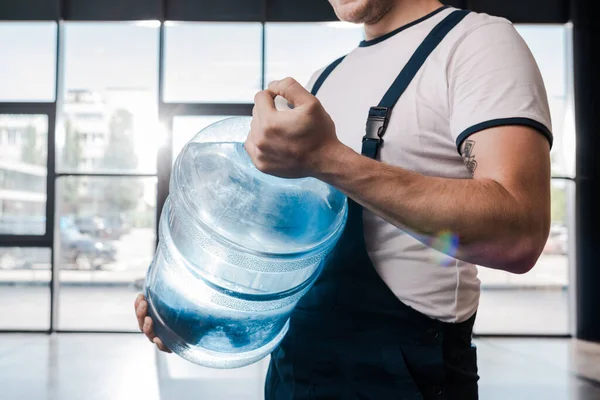 Cropped view of delivery man holding heavy gallon with water — Stock Photo