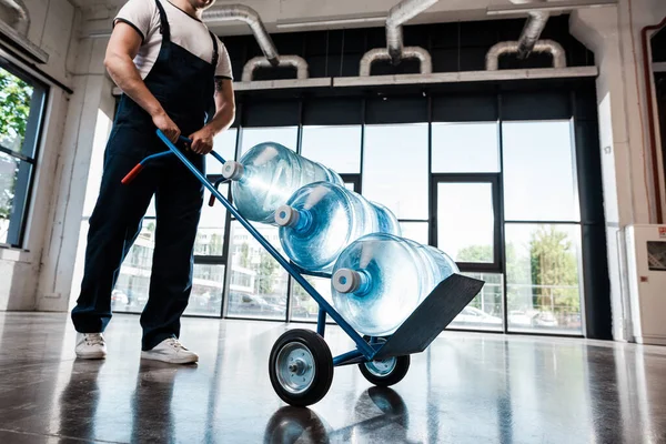 Cropped view of delivery man holding hand truck with bottles of purified water — Stock Photo