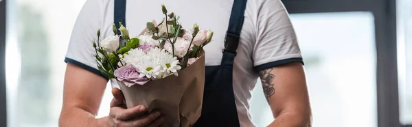 Panoramic crop of delivery man holding bouquet of flowers — Stock Photo