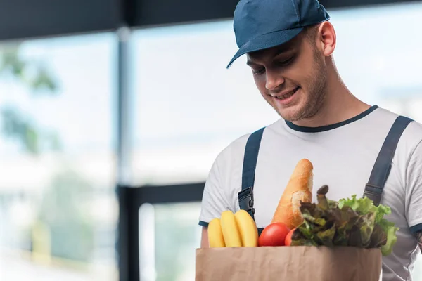 Cheerful delivery man holding paper bag with fresh groceries — Stock Photo