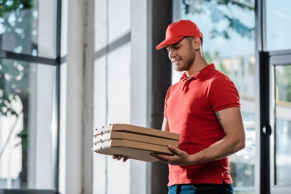 Щасливий чоловік доставки в кепці дивиться на коробки для піци — стокове фото