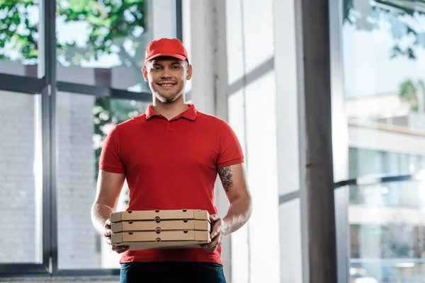 Hombre de entrega feliz en gorra y uniforme sosteniendo cajas de pizza - foto de stock