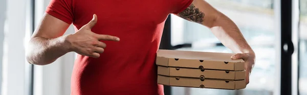 Cosecha horizontal del repartidor hombre apuntando con el dedo a las cajas de pizza - foto de stock