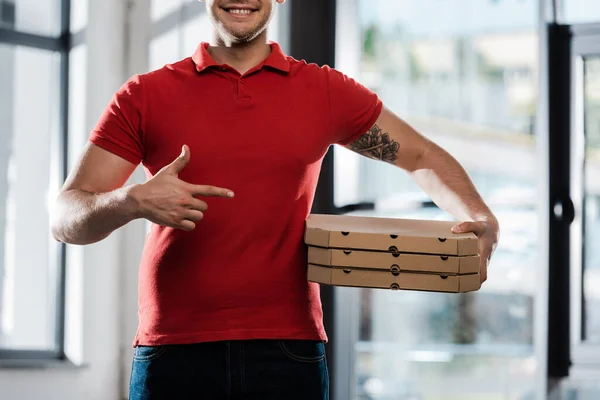 Recortado vista de feliz repartidor hombre señalando con el dedo en cajas de pizza - foto de stock