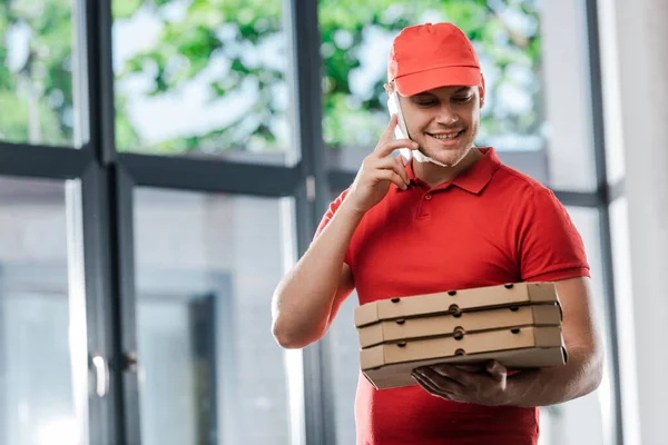 Heureux livreur homme en chapeau parler sur smartphone et tenant des boîtes à pizza — Photo de stock