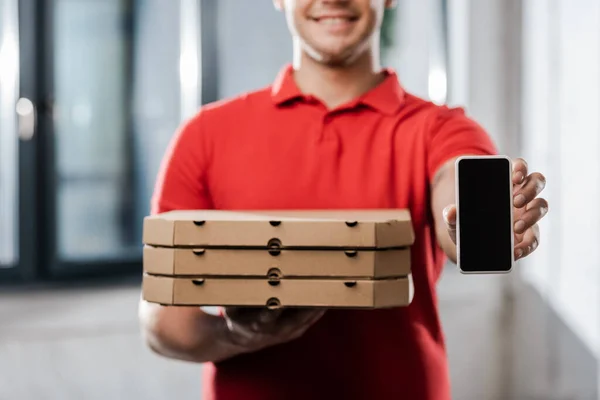 Vue recadrée du livreur heureux dans le chapeau tenant smartphone avec écran vierge et boîtes à pizza — Photo de stock