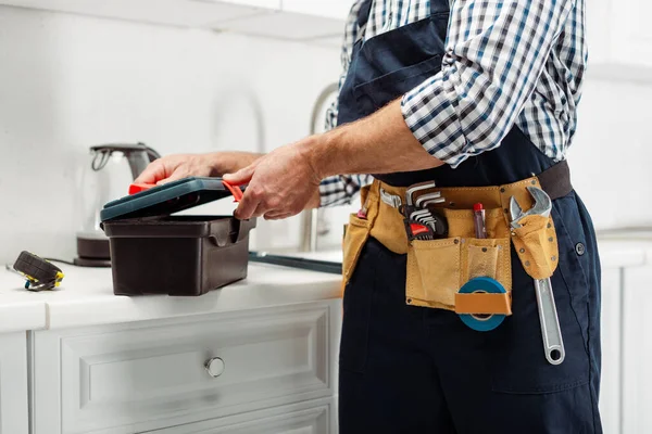 Cropped view of plumber in overalls opening toolbox on worktop in kitchen — Stock Photo