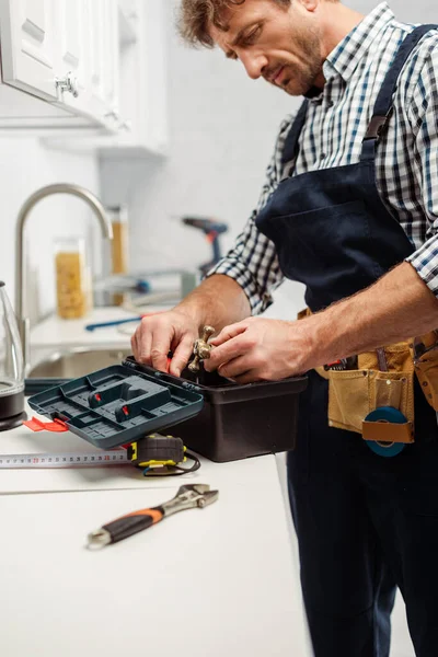 Selective focus of plumber holding handle of faucet near open toolbox in kitchen — Stock Photo