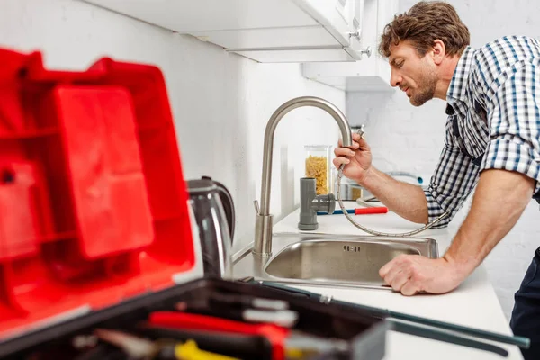 Foco selectivo del fontanero que sostiene la tubería metálica cerca del grifo de la cocina y la caja de herramientas - foto de stock