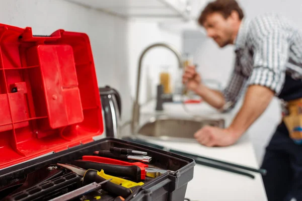 Focus selettivo dello strumento in cassetta degli attrezzi e idraulico che lavora in cucina — Foto stock