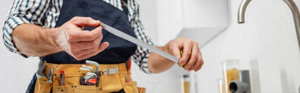 Panoramic shot of plumber holding industrial measuring tape in kitchen — Stock Photo