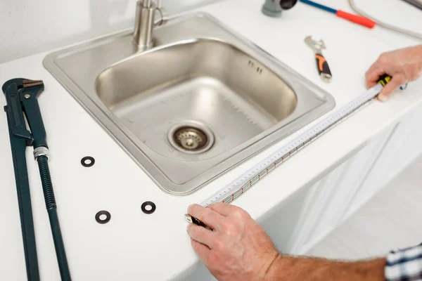 Cropped view of plumber measuring worktop with industrial measuring tape near tools in kitchen — Stock Photo