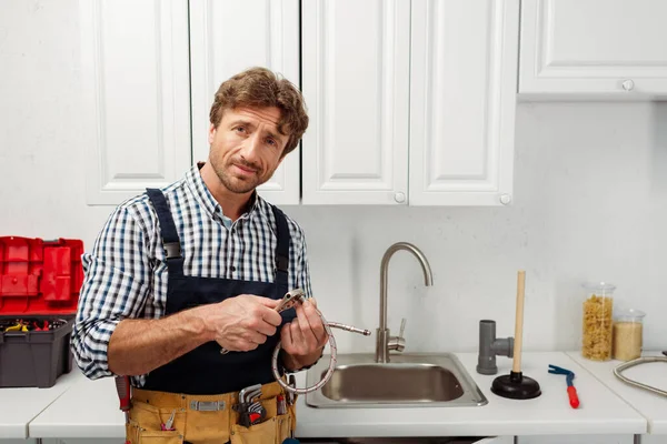 Encanador segurando tubo de metal e chave enquanto trabalhava na cozinha — Fotografia de Stock