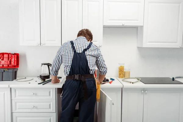 Back view of plumber in overalls working in kitchen — Stock Photo
