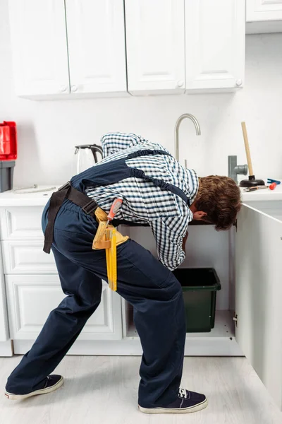 Back view of plumber in overalls fixing sink in kitchen — Stock Photo