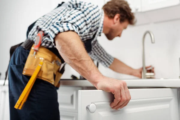 Selective focus of plumber in tool belt repairing kitchen faucet — Stock Photo