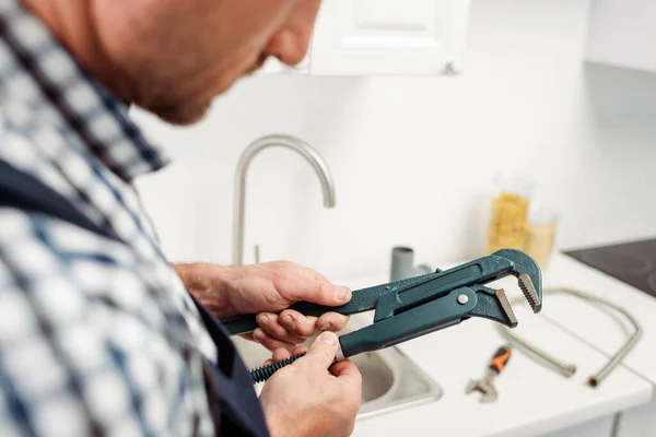 Cropped view of plumber holding pipe wrench in kitchen — Stock Photo