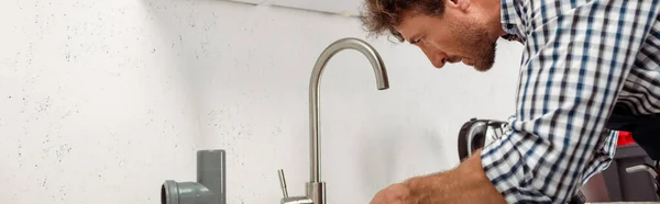 Panoramic shot of plumber fixing kitchen faucet near plastic pipe — Stock Photo