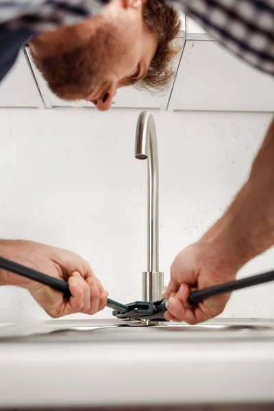 Вибірковий фокус водопровідника, який тримає трубний гайковий ключ під час кріплення кухонного крана — стокове фото