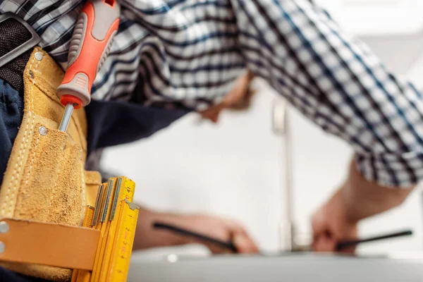 Selective focus of plumber in tool belt working in kitchen — Stock Photo