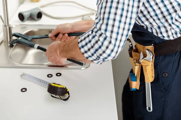 Cropped view of repairman fixing faucet with pipe wrench near tools on kitchen worktop — Stock Photo