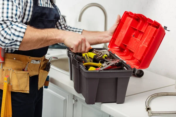 Vue recadrée du travailleur en salopette ouvrant la boîte à outils sur le plan de travail de la cuisine — Photo de stock