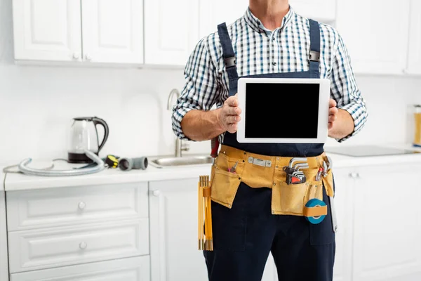 Vista recortada del fontanero en el cinturón de herramientas que sostiene la tableta digital en la cocina - foto de stock