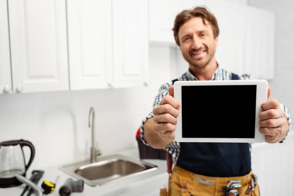 Foyer sélectif de plombier souriant montrant tablette numérique avec écran blanc dans la cuisine — Photo de stock