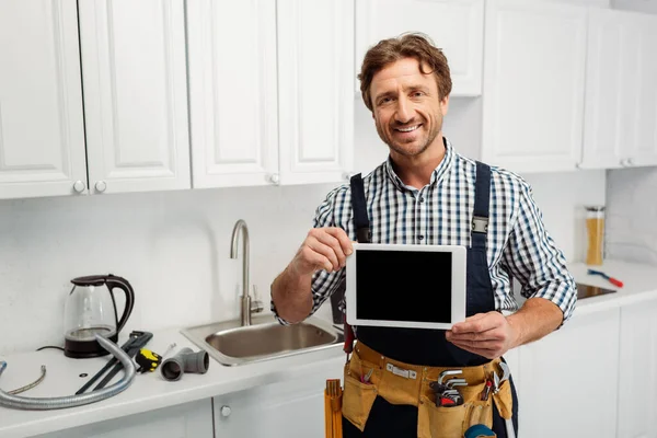 Trabajador sonriente sosteniendo tableta digital con pantalla en blanco cerca de herramientas en la encimera de la cocina - foto de stock