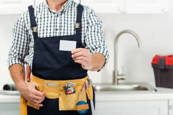 Vista recortada del fontanero en cinturón de herramientas que sostiene la tarjeta vacía en la cocina - foto de stock