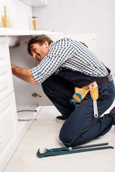 Side view of plumber repairing sink near pipe wrench in kitchen — Stock Photo