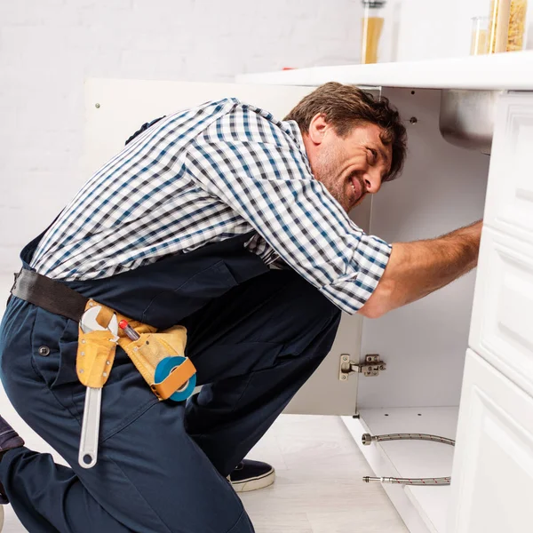 Seitenansicht des Reparateurs in Uniform und Werkzeuggürtel zur Befestigung der Spüle — Stockfoto