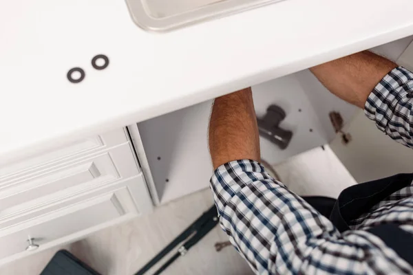 Vista ritagliata di idraulico che fissa il lavandino in cucina vicino agli strumenti sul pavimento — Foto stock