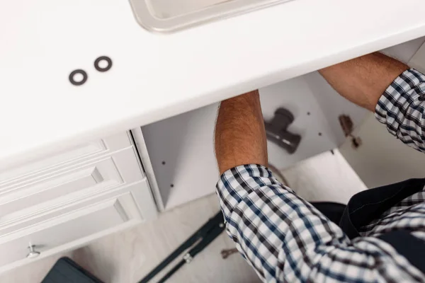 Cropped view of plumber fixing sink in kitchen near tools on floor — Stock Photo