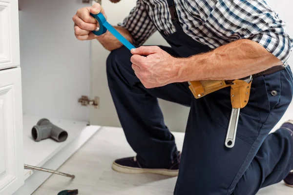 Vista recortada del plomero sosteniendo cinta aislante mientras fija el fregadero en la cocina - foto de stock