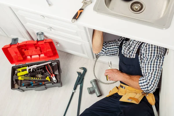 Hochwinkelansicht der Klempner Befestigung Spüle mit einer Zange in der Nähe von Instrumenten und Werkzeugkiste auf dem Boden — Stockfoto