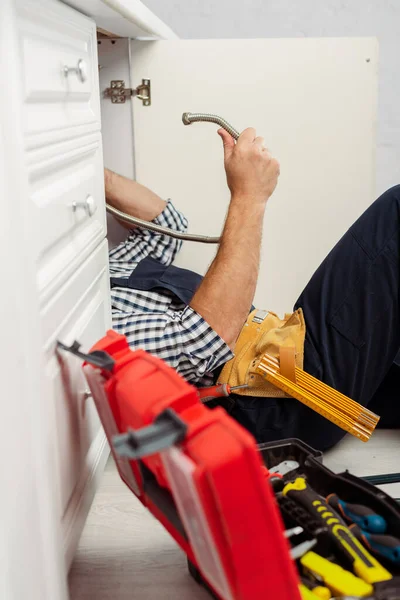 Selektiver Fokus des Arbeiters, der Metallrohr in der Nähe des offenen Werkzeugkastens hält, während er die Küchenspüle fixiert — Stockfoto