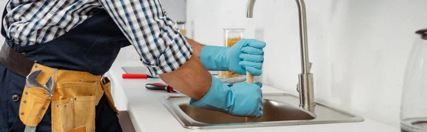 Panorâmica tiro de encanador em luvas de borracha usando êmbolo durante a limpeza pia da cozinha — Fotografia de Stock