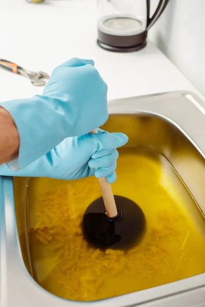 Cropped view of plumber in rubber gloves cleaning kitchen sink with plunger — Stock Photo