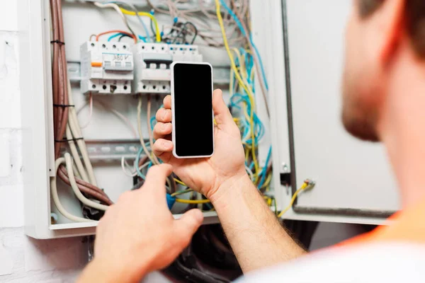 Selective focus of electrician holding smartphone near electrical distribution box — Stock Photo