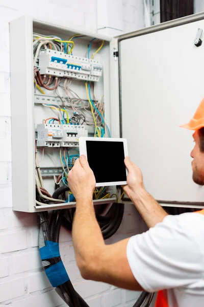 Enfoque selectivo del electricista sosteniendo tableta digital con pantalla en blanco cerca del panel eléctrico - foto de stock