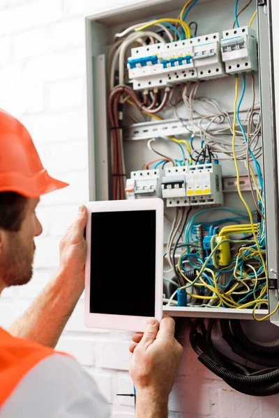 Enfoque selectivo del electricista sosteniendo tableta digital con pantalla en blanco cerca de la caja de distribución eléctrica - foto de stock