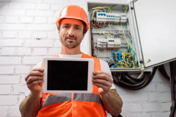 Selective focus of handsome electrician showing digital tablet with blank screen near electrical box — Stock Photo