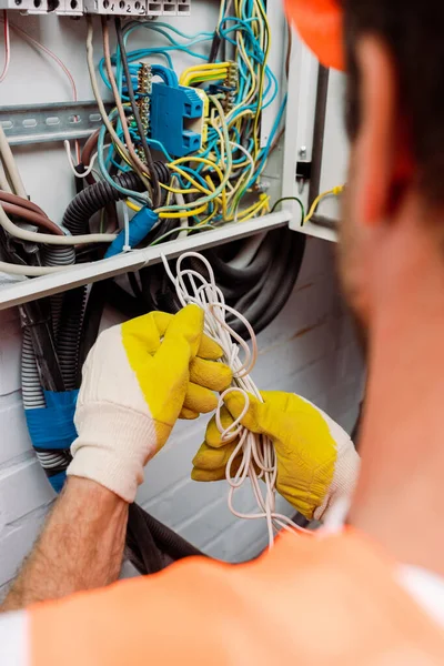 Selektiver Fokus des Elektrikers in Handschuhen, die Drähte halten, während er Stromverteilerkasten fixiert — Stockfoto