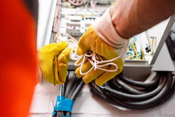 Cropped view of electrician in gloves holding wires near electrical box — Stock Photo