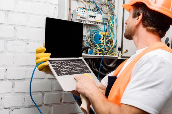 Selective focus of electrician using laptop near electrical distribution box — Stock Photo